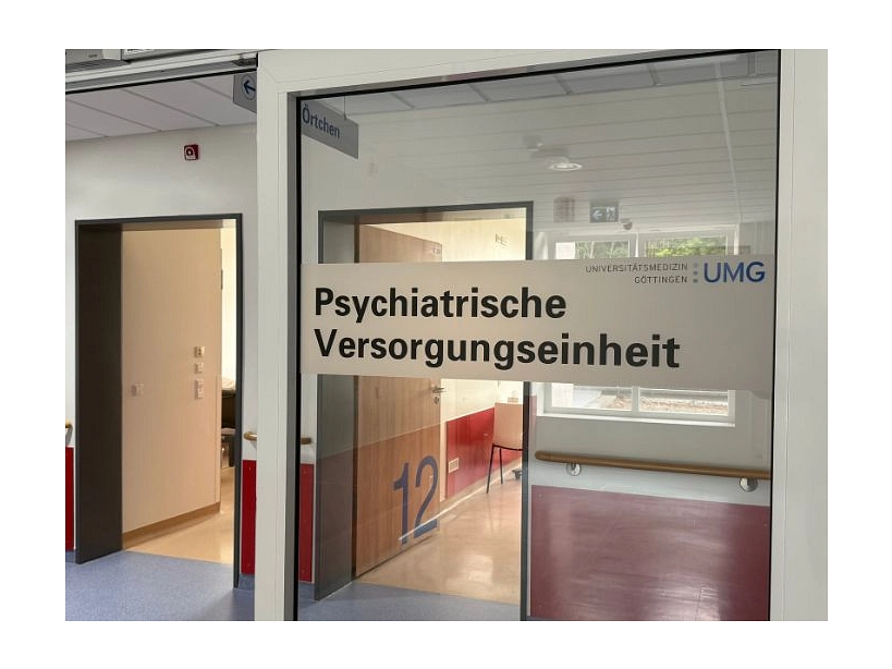 Zu sehen ist der Eingang der Psychiatrischen Versorgungseinheit der UMG im BürgerGesundheispark, es steht "Psychatrische Versorgungseinheit" an einer Glastür. Zu sehen ist auch das Logo der Universitätsmedizin Göttingen.
