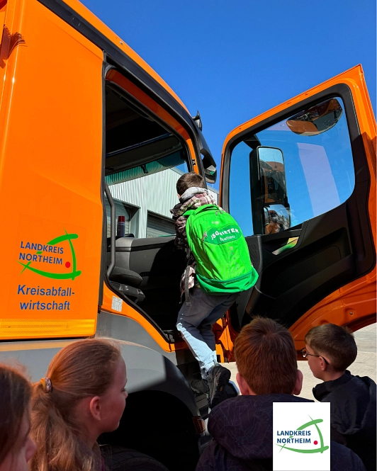 Zu sehen ist ein Junge, der in die Fahrerkabine eines Müllfahrzeuges einsteigt.