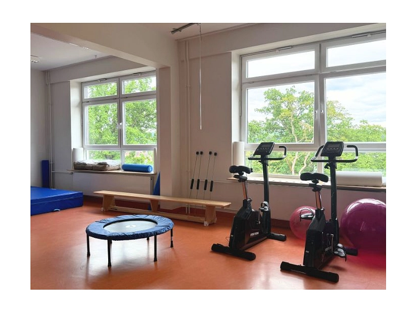 Zu sehen ist ein Sportraum mit Ergometern, kleinem Trampolin, Bällen etc.