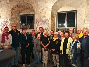 Das Foto zeigt eine Gruppe von etwa 15 Personen, die in einem historischen Gewölberaum mit Steinwänden und hohen Fenstern zusammenstehen. Einige tragen dunkle Polohemden mit einem gelben Emblem, andere Freizeitkleidung in helleren Farben. Im Hintergrund sind Kunstwerke mit floralen Motiven an den Wänden zu sehen.&nbsp;&copy;&nbsp;Irene Söffker
