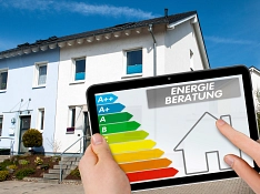 Im Vordergrund ist ein Tablet zu sehen, auf dem die Skizze eines Hauses und die Energieklassen zu sehen sind. Darüber steht "Energieberatung". Im Hintergrund des Bildes sind zwei Reihenhäuser zu sehen.&nbsp;&copy;&nbsp;AdobeStock