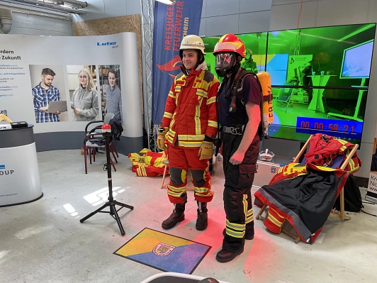 Zwei Messeteilnehmer posieren in der Arbeitskleidung der Feuerwehr.