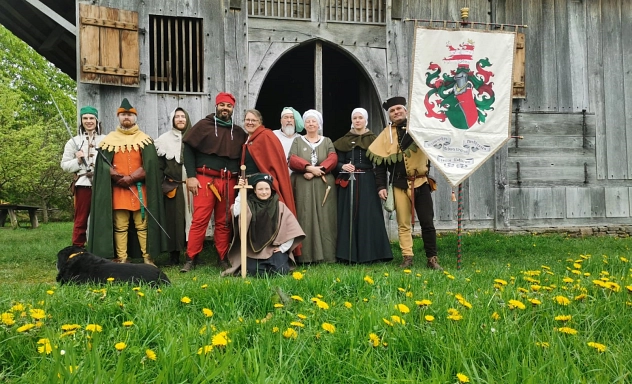 Casta Gladiorum - Mittelalterhaus Nienover Auf dem Bild ist eine Personengruppe in Mittelalterkleidung auf einer grünen Wiese abgebildet.