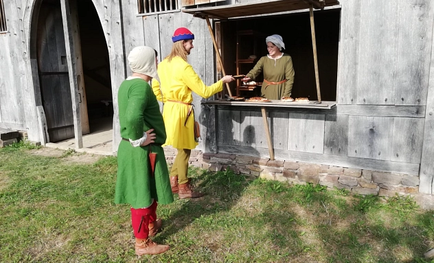 Das Rudel e. V. im Mittelalterhaus Drei mittelalterlich gekleidete Personen stehen vor dem Mittelalterhaus Nienover. Eine Person reicht an einem geöffneten Fenster etwas an eine weitere Person weiter.
