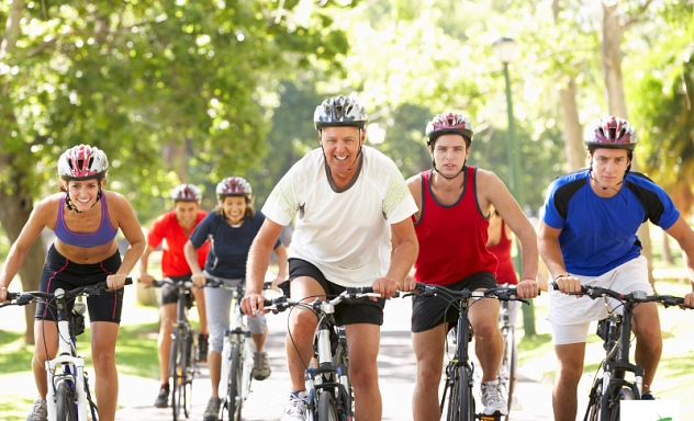 Fahrradtag Eine Gruppe Männer und Frauen radelt durch eine sommerliche Landschaft. Die Personen tragen sportliche Kleidung und Fahrradhelme. Alle schauen freundlich in die Kamera.