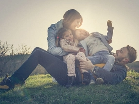 Das Symbolbild zeigt Eltern mit zwei Kindern, die auf einer Wiese spielen.&nbsp;&copy;&nbsp;canva