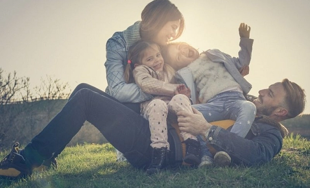 Familie, Kinder, Eltern Das Symbolbild zeigt Eltern mit zwei Kindern, die auf einer Wiese spielen.
