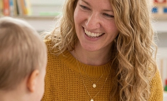Eine Frau sitzt an einem Tisch einem kleinen Kind gegenüber und hält ein Spielzeug in der Hand.