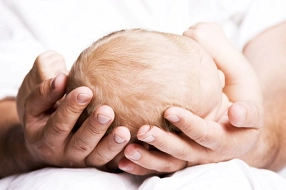 Man sieht den Kopf eines Babys, der sanft in den Händen des Vaters liegt.&nbsp;&copy;&nbsp;istock/Lloret