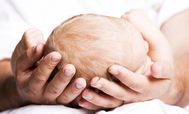 Frühe Hilfen Titelbild Man sieht den Kopf eines Babys, der sanft in den Händen des Vaters liegt.