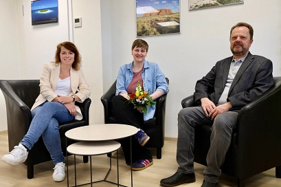 Zwei Frauen und ein Mann sitzen in schwarzen Sesseln in einem hellen Raum und blicken in die Kamera. Die Frau in der Mitte hält einen bunten Blumenstrauß. Zwischen ihnen steht ein kleiner runder Tisch, im Hintergrund hängen Landschaftsbilder an der Wand.&nbsp;&copy;&nbsp;Landkreis Northeim