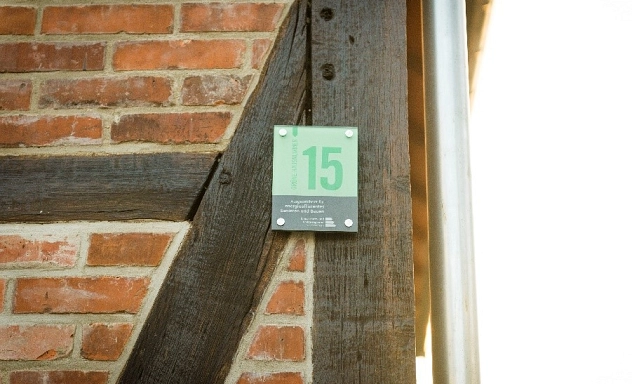Grüne Hausnummer Zu sehen ist die Mauer eines Fachwerkhauses an dem eine "Grüne Hausnummer" befestigt ist.