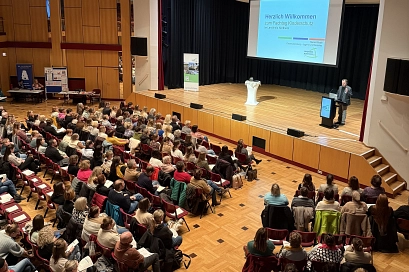 Zu sehen ist die Stadthalle in Northeim, der Besucherraum ist mit Menschen gefüllt. Auf der Bühne steht Der Dezernent für Jugend und Soziales des Landkreises Northeim, Harald Rode. Auf der Präsentationsfolie im Hintergrund ist "Fachtag Kinderschutz" zu lesen.&nbsp;&copy;&nbsp;Landkreis Northeim