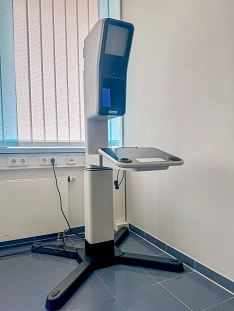 Eine moderne Lichtbildstation in einem Behördenraum. Das Gerät steht auf einem stabilen schwarzen Fuß und verfügt über einen Monitor, eine Kameraeinheit und eine integrierte Ablagefläche. Im Hintergrund befinden sich eine Fensterjalousie und mehrere Steckdosen an der Wand.&nbsp;&copy;&nbsp;Landkreis Northeim