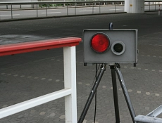 Auf dem Bild ist ist eine mobile Messanlage zu sehen, links daneben ein weiß-rotes Geländer. Im Hintergrund befindet sich ein Parkplatz und eine Straße.