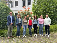 Netzwerktreffen Klimaschutz Einbeck Sieben Teilnehmende des Netzwerktreffens stehen im Außenbereich vor dem Rathaus Einbeck. Im Hintergrund sind das Gebäude, Bäume und blühende Sträucher zu sehen.