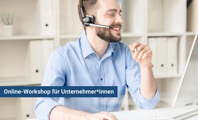 Zu sehen ist ein junger Mann mit blauem Hemd, der mit einem Headset vor einem Computer sitzt.