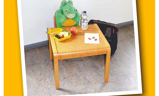 Postmappe Zahngesundheit 1 Zu sehen ist ein Foto von einer gelben Mappe, auf der mit Buchstaben in Regenbogenfarben das Wort Postmappe steht. Vorne auf der Mappe ist ein Foto von einem Krokodil-Kuscheltier zu sehen, das mit einer aufgeklappten gelben Brotdose mit einer Gurke, einem Käüsebrot, einer Mohrrübe sowie einem Apfel und einer Flasche Wasser und einem Blatt Papier an einem kleinen Tisch sitzt. Daneben steht ein Rucksack.
Unter dem Foto befindet sich ein weißes Feld, auf dem am unteren Rand das Wort "Name" in Gelb steht.