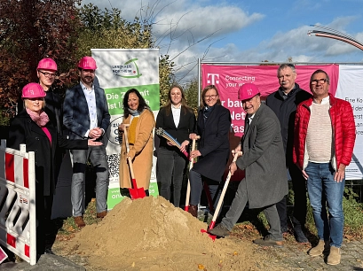 Spatenstich Breitbandausbau Telekom 2025 Zu sehen sind (v.l.n.r.): Sabine Köhler (Regionalmanagerin der Telekom), André Zehl (zuständiger Technischer Leiter der Telekom), Steffen Weißhuber (Konzernbevollmächtigter der Telekom), Astrid Klinkert-Kittel (Landrätin), Annkathrin Martin (Fördermittelberaterin aconium), Sabine Michalek (Bürgermeisterin Einbeck), Torsten Bauer (Bürgermeister Uslar), Gerald Wucherpfennig (Bürgermeister Flecken Bodenfelde), Volker Fuchs (Allgemeiner Vertreter des Bürgermeisters Stadt Dassel). Sie stehen draußen vor verschiedenen Roll-Ups von Telekom und Landkreis. Drei Personen halten einen Spaten in der Hand und stechen ihn symbolisch in einen Sandhaufen. Drei Personen tragen außerdem magentafarbene Bauhelme. © Landkreis Northeim