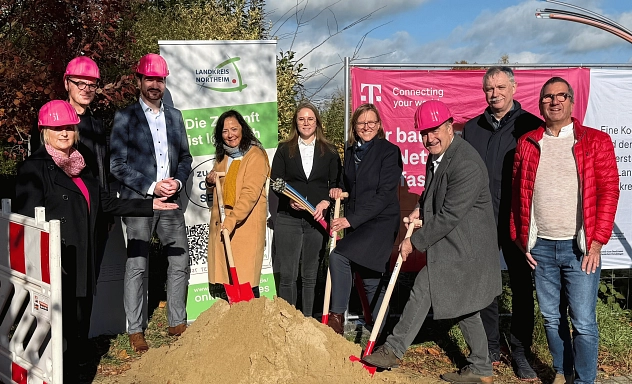 Spatenstich Breitbandausbau Telekom 2025 Zu sehen sind (v.l.n.r.): Sabine Köhler (Regionalmanagerin der Telekom), André Zehl (zuständiger Technischer Leiter der Telekom), Steffen Weißhuber (Konzernbevollmächtigter der Telekom), Astrid Klinkert-Kittel (Landrätin), Annkathrin Martin (Fördermittelberaterin aconium), Sabine Michalek (Bürgermeisterin Einbeck), Torsten Bauer (Bürgermeister Uslar), Gerald Wucherpfennig (Bürgermeister Flecken Bodenfelde), Volker Fuchs (Allgemeiner Vertreter des Bürgermeisters Stadt Dassel). Sie stehen draußen vor verschiedenen Roll-Ups von Telekom und Landkreis. Drei Personen halten einen Spaten in der Hand und stechen ihn symbolisch in einen Sandhaufen. Drei Personen tragen außerdem magentafarbene Bauhelme.