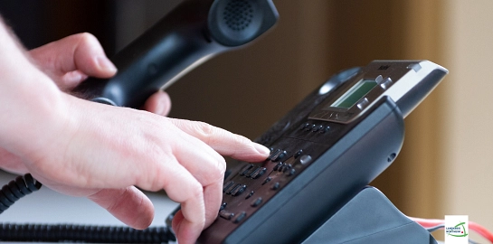 Zu sehen ist eine Hand die einen Hörer hält und eine andere Hand die auf einem Telefon wählt.