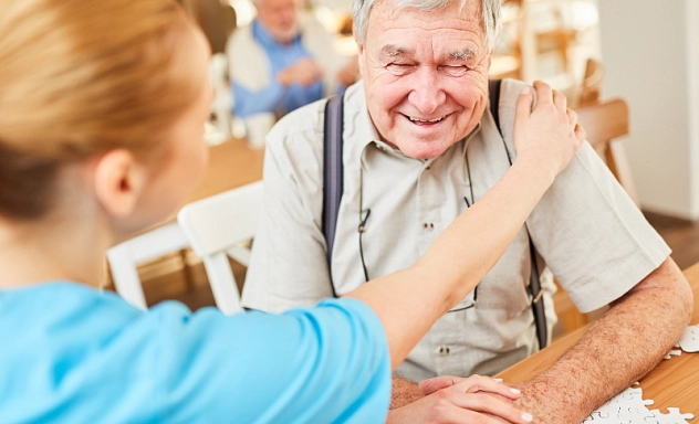 Auf dem Bild ist eine Pflegerin zu sehen, die einem alten Mann ihre Hand auf die Schulter legt.