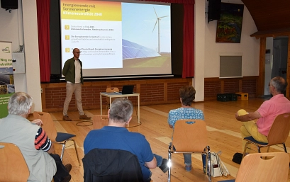 Zu sehen ist ein Saas mit Stühlen auf denen Personen sitzen, sie sind von hinten zu sehen. Vorne steht ein Mann vor einer Leinwand auf der eine Powerpoint Präsentation läuft.&nbsp;&copy;&nbsp;Landkreis Northeim