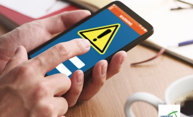 Zu sehen ist eine Hand die ein Smartphone hält. Auf dessen Display ist ein Achtung-Zeichen zu sehen.