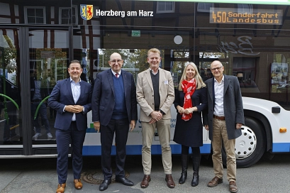 Fünf Personen, vier Männer und eine Frau, stehen vor einem weißen Linienbus mit der Aufschrift ‚Herzberg am Harz‘ und der Linienanzeige ‚450 Sonderfahrt Landesbus‘. Die Gruppe besteht aus drei Männern in Anzügen, einer Frau mit rotem Schal und einem weiteren Mann im Mantel. Sie lächeln in die Kamera, der Bus dient als Hintergrund.&nbsp;&copy;&nbsp;ZVSN